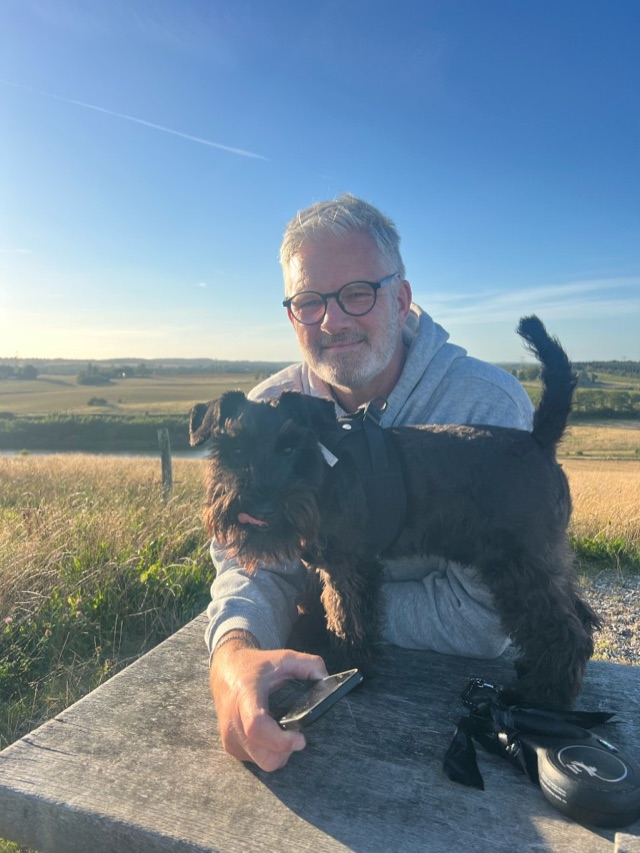 Jan Trane Roebel udendørs med sin dværgschnauzer Ejner i det danske landskab
